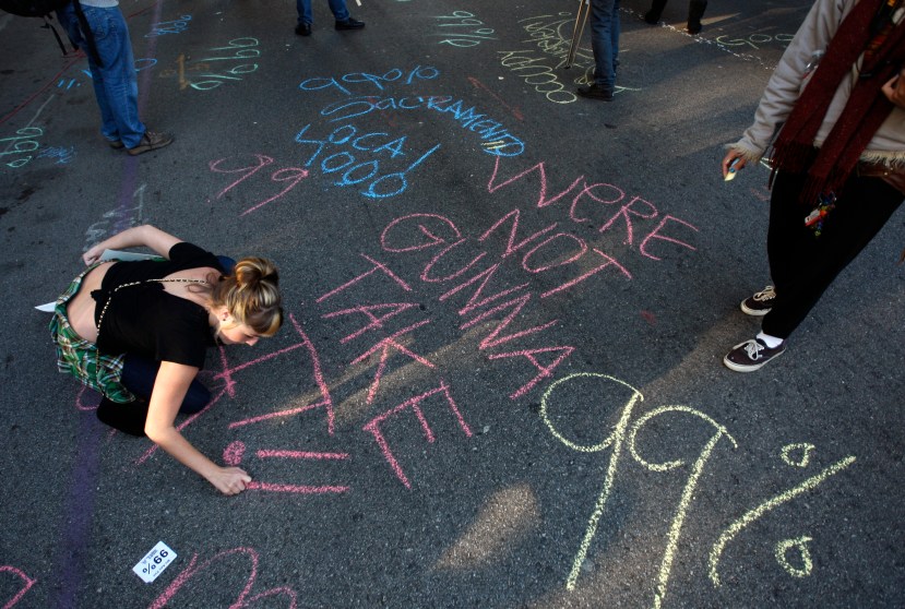 A protester uses a piece of chalk to write slogans on the street during a protest in Los Angeles