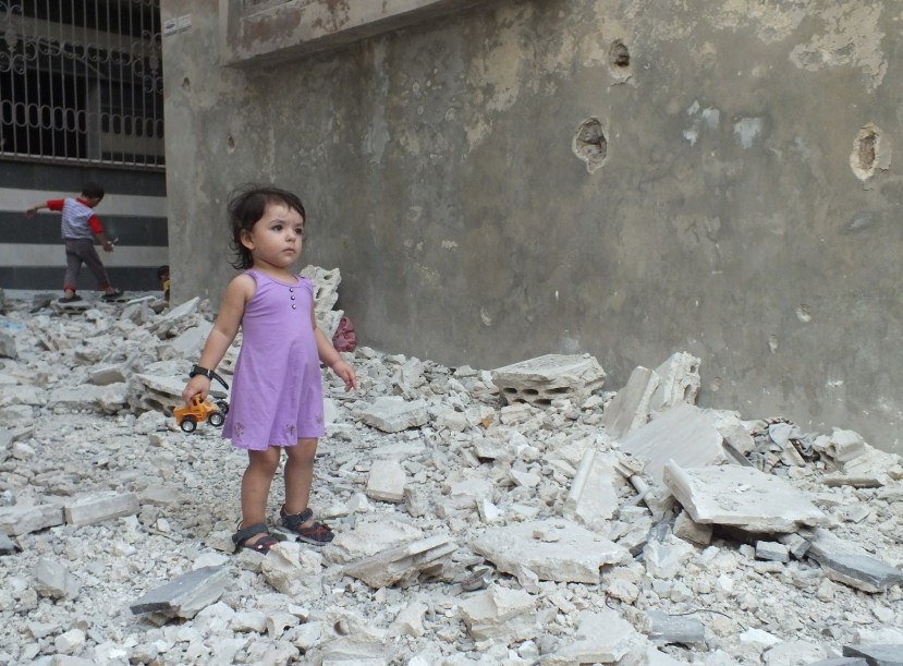A girl stands on debris next to a damaged building at a besieged area of Homs